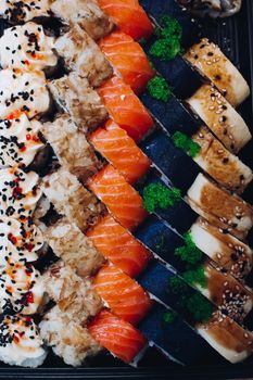 Colorful delicious mouthwatering sushi set laying on the plate including different ingredients: fish, caviar, rice, cucumber, salmon, soy sauce, wasabi, sesame seeds. An interesting presentation.