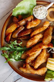 Clay plate full of appetizers served with goldy chicken nuggets cooked with chrispy crust, delicious canapes with herring and cherry tomatoes, garlic sauce, decorated with fresh salad and cheese.