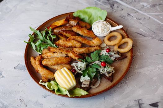 Clay plate full of appetizers including goldy chicken nuggets with chrispy crust, delicious canapes with herring and cherry tomatoes, served with garlic sauce, decorated with salad leaves and cheese.