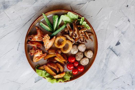 Clay plate full of appetizers including goldy chicken nuggets with chrispy crust, delicious canapes with herring and cherry tomatoes, served with garlic sauce, decorated with salad leaves and cheese.