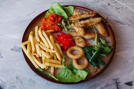 Tasty appetizers for big company of friends drinking beer: goldy chicken nuggets, fried potatoes, green salad leaves and fresh cucumbers. Standing on white table. Looking delicious, mouthwatering.