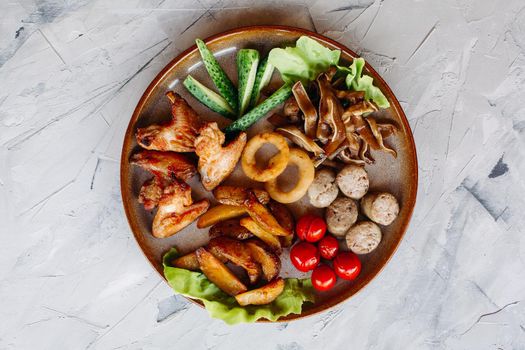 Clay plate full of appetizers including goldy chicken nuggets with chrispy crust, delicious canapes with herring and cherry tomatoes, served with garlic sauce, decorated with salad leaves and cheese.