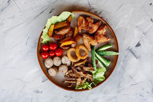 Clay plate full of appetizers including goldy chicken nuggets with chrispy crust, delicious canapes with herring and cherry tomatoes, served with garlic sauce, decorated with salad leaves and cheese.