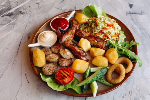 Delicious restaurant appetizers set for beer. vegetable salad, boiled potatoes, grilled chicken legs, roasted onion, sausages, cucmbers, tomatoes and sauces - ketchup and mayo laying on clay plate.