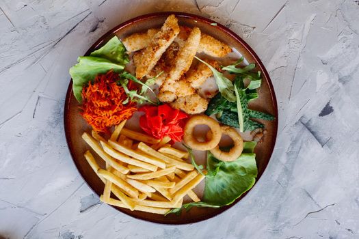 Tasty restaurant appetizers for big company including goldy chicken nuggets, fried potatoes, green salad leaves and fresh cucumbers. Standing on white table. Looking delicious, mouthwatering.