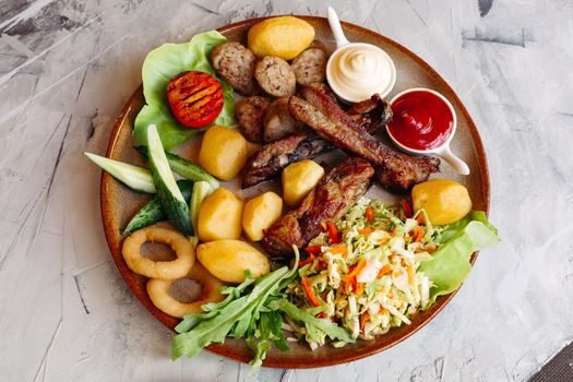 Delicious restaurant appetizers set for beer. vegetable salad, boiled potatoes, grilled chicken legs, roasted onion, sausages, cucmbers, tomatoes and sauces - ketchup and mayo laying on clay plate.