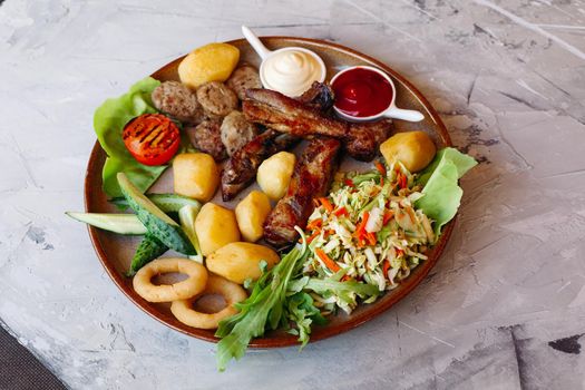 Delicious restaurant appetizers set for beer. vegetable salad, boiled potatoes, grilled chicken legs, roasted onion, sausages, cucmbers, tomatoes and sauces - ketchup and mayo laying on clay plate.