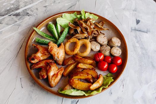 Clay plate full of appetizers including goldy chicken nuggets with chrispy crust, delicious canapes with herring and cherry tomatoes, served with garlic sauce, decorated with salad leaves and cheese.