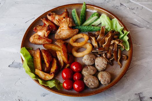 Clay plate full of appetizers including goldy chicken nuggets with chrispy crust, delicious canapes with herring and cherry tomatoes, served with garlic sauce, decorated with salad leaves and cheese.