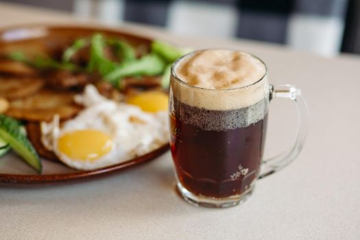 Beer cup standing near appetizers plate. Dark beer with thick high foam. Standing on smooth wooden surface of restaurant's or pub table. Looking mouthwatering. Cold and fresh. For friends company.