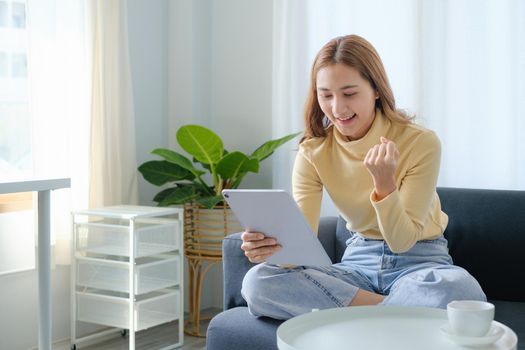 Woman enjoy with content social media application on digital tablet sitting on sofa at home