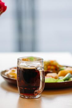 Beer cup standing near appetizers plate. Dark beer with thick high foam. Standing on smooth wooden surface of restaurant's or pub table. Looking mouthwatering. Cold and fresh. For friends company.