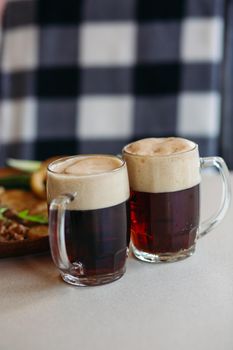 Two big glass cups full of foamy cold beer standing on light smooth table surface in restaurant or pub. Big plate with delicious appetizers like potato puncakes and fried eggs standing on background.