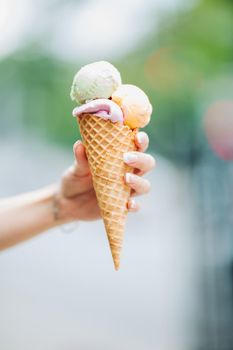 Tender woman's hand keeping delicious colorful ice cream. Lookinf very tasty, sweet, mouthwatering, perfect for summer heat while sunny day. Pretty nails with professional french manicure. Soft focus.