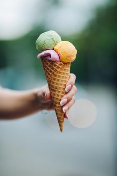 Crop of woman's hand holding delicious colorful ice cream with three colors. Close up of tasty, sweet, mouthwatering, perfect for summer heat while sunny day. Summertime vibes and sweet food.