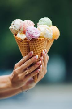 Crop of woman's hand holding delicious colorful ice cream, looking tasty, sweet, mouthwatering, perfect for summer heat while sunny day. Pretty nails with professional french manicure. Food concept.