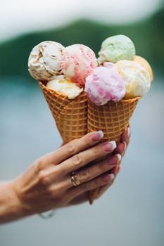 Crop of woman's hand holding delicious colorful ice cream, looking tasty, sweet, mouthwatering, perfect for summer heat while sunny day. Pretty nails with professional french manicure. Food concept.