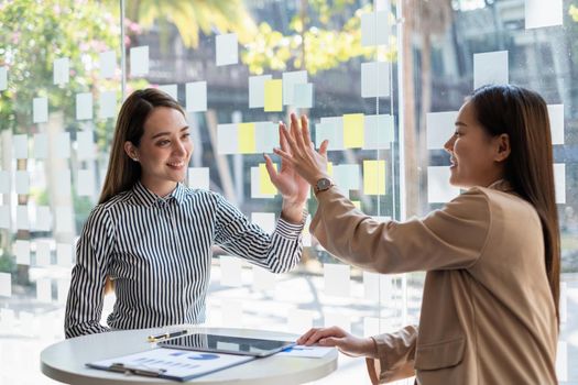 Asian businesswoman and her partners give each other high fives as they celebrate a successful team building project