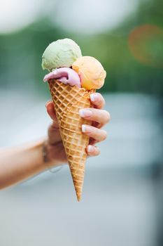 Tender woman's hand keeping delicious colorful ice cream. Lookinf very tasty, sweet, mouthwatering, perfect for summer heat while sunny day. Pretty nails with professional french manicure. Soft focus.