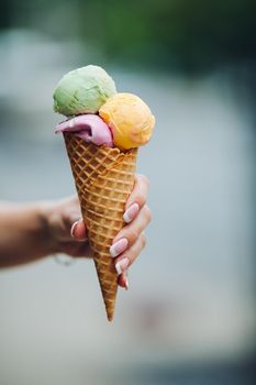 Crop of woman's hand holding delicious colorful ice cream with three colors. Close up of tasty, sweet, mouthwatering, perfect for summer heat while sunny day. Summertime vibes and sweet food.