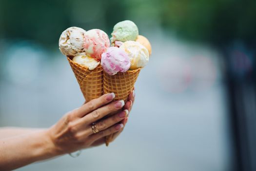 Crop of woman's hand holding delicious colorful ice cream, looking tasty, sweet, mouthwatering, perfect for summer heat while sunny day. Pretty nails with professional french manicure. Food concept.