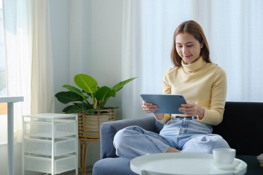 Woman enjoy with content streaming movies or social media application on digital tablet sitting on sofa at home