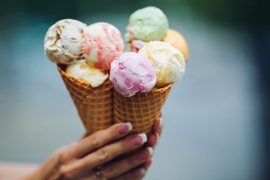 Crop of woman's hand holding delicious colorful ice cream, looking tasty, sweet, mouthwatering, perfect for summer heat while sunny day. Pretty nails with professional french manicure. Food concept.