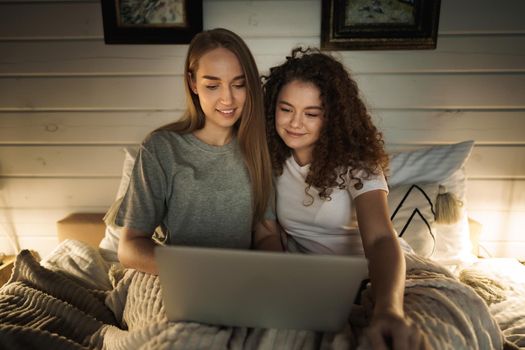 Two beautiful women lying in bed and watching movies on laptop at home
