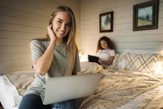 Two beautiful women lying in bed, holding and watching laptop