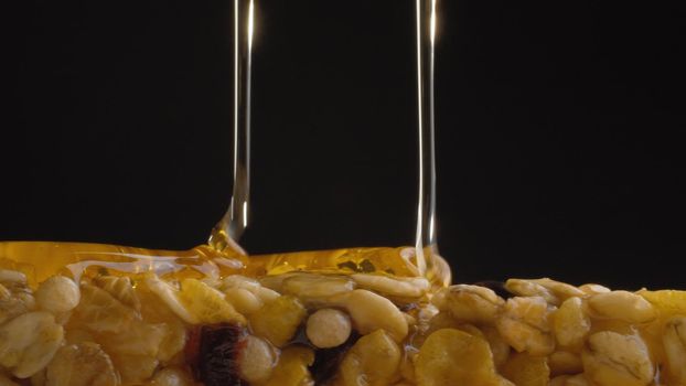 Extreme close up fresh honey pouring on a cereal bar, muesli on black background. Healthy energy fitness food