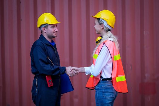 Technician man and woman shake hand together in front of cargo container with concept of successful in shipping business.