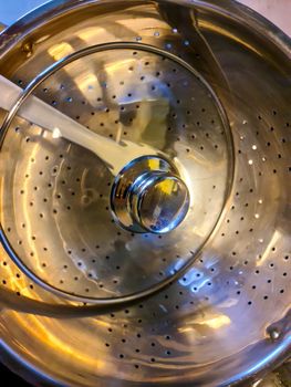 High angle view of a chrome pasta strainer in a pot on a stove