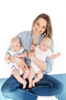 Picture of cheerful young caucasian female sits with her children, smiles and hugs them