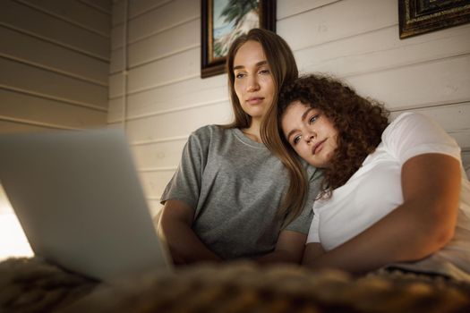 Two beautiful women lying in bed and watching movies on laptop at home