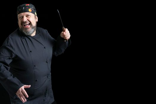 Portrait of laughing and cheerful cook with knife in hand with black background and copy space on the right side. Expressions of concept.