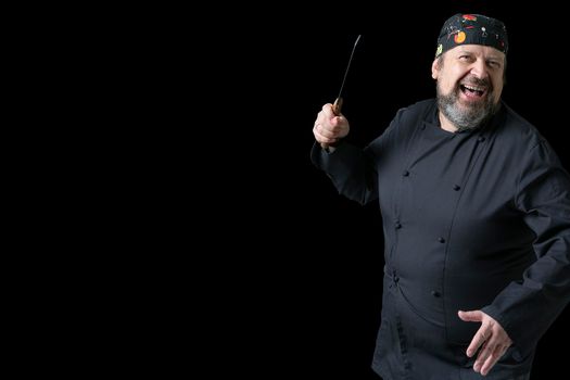 Portrait of laughing and cheerful cook with knife in hand with black background and copy space on left side. Expressions of concept.