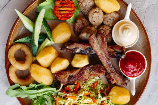 Colorful top view of tasty restaurant meal. clay plate including sausages, cucmbers, boiled potatoes, grilled chicken legs, roasted onion, vegetable salad served with ketchup and mayo.