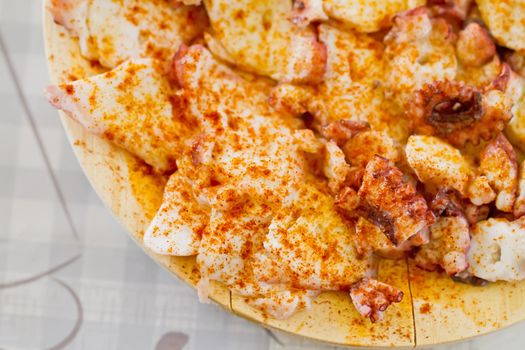 cooked octopus slices dressed with paprika over wooden plate, top view