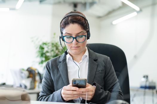 The call center operator gets bored and uses a smartphone at the workplace. A business woman is sitting at her desk and typing on a mobile phone.
