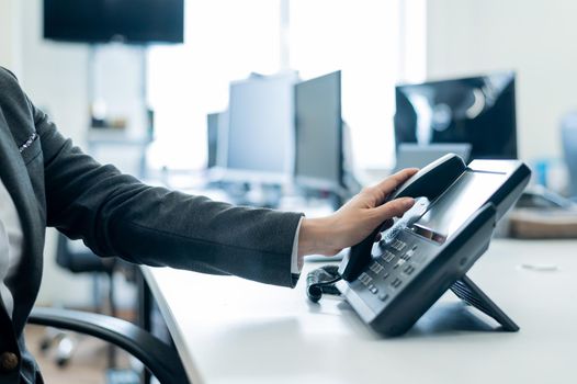 Close-up of a female employee's hand on a landline phone. Woman picks up a push-button telephone at the workplace in the office.