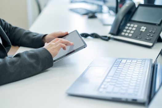 Close-up of the hands of a female secretary with a digital tablet. Faceless woman at her desk in the office