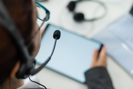 Rear view of a woman in a headset using a digital tablet while sitting at a desk. Friendly female support service operator at work