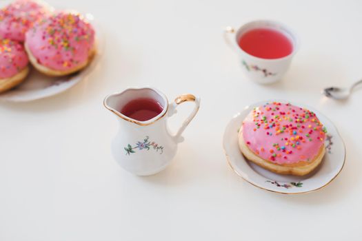 holiday, birthday party composition with colorful pink glazed donuts on white table, flatlay top view. 