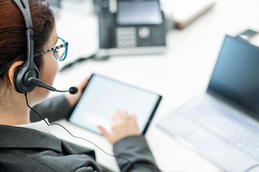 A business woman with a headset holds a digital tablet while sitting at a desk.