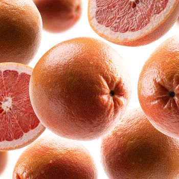 Whole and cut grapefruits levitate on a white background.
