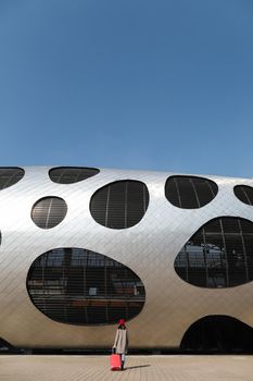 young woman with a red travel suitcase by the futuristic facade of modern architecture. Travel