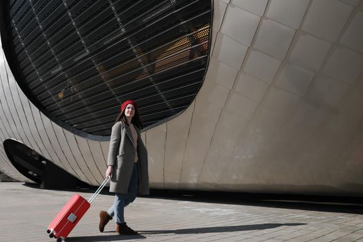 young woman with a red travel suitcase by the futuristic facade of modern architecture. Travel