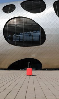 red travel suitcase by the futuristic facade of modern architecture