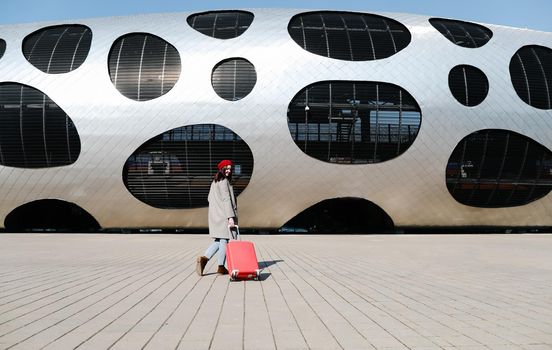 young woman with a red travel suitcase by the futuristic facade of modern architecture. Travel concept
