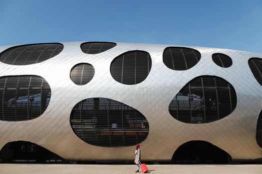 young woman with a red travel suitcase by the futuristic facade of modern architecture. Travel